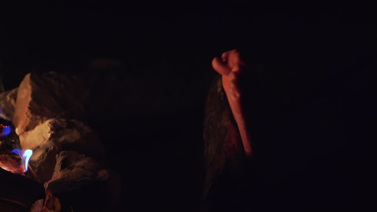 hembra calentando sus pies cerca de un fuego de campamento en una noche