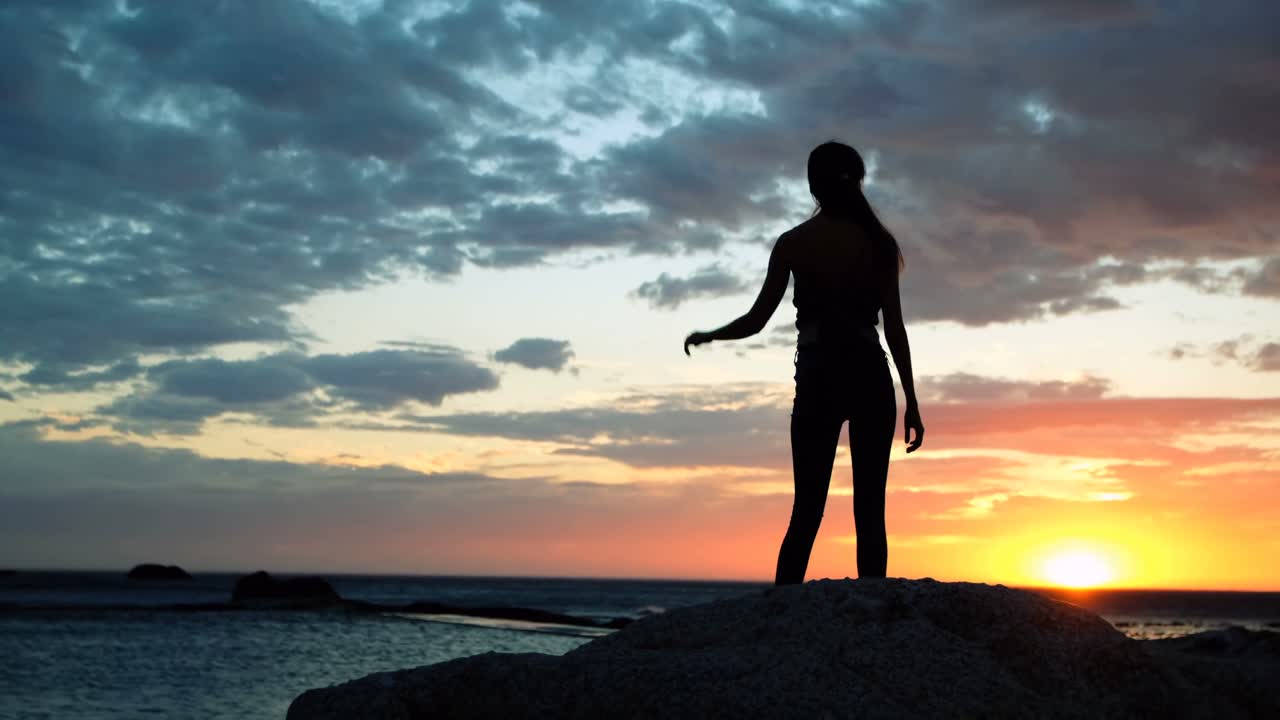 저녁 4k 동안 해변에서 바위 위에 서있는 여성