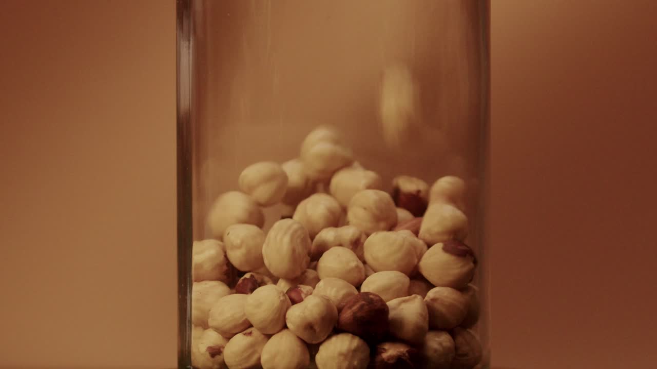 Slow motion of falling hazelnuts into glass Jar - light brown background