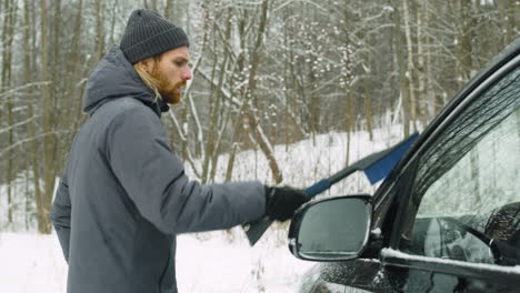 man cleaning his car from snow with a brush in a winter day