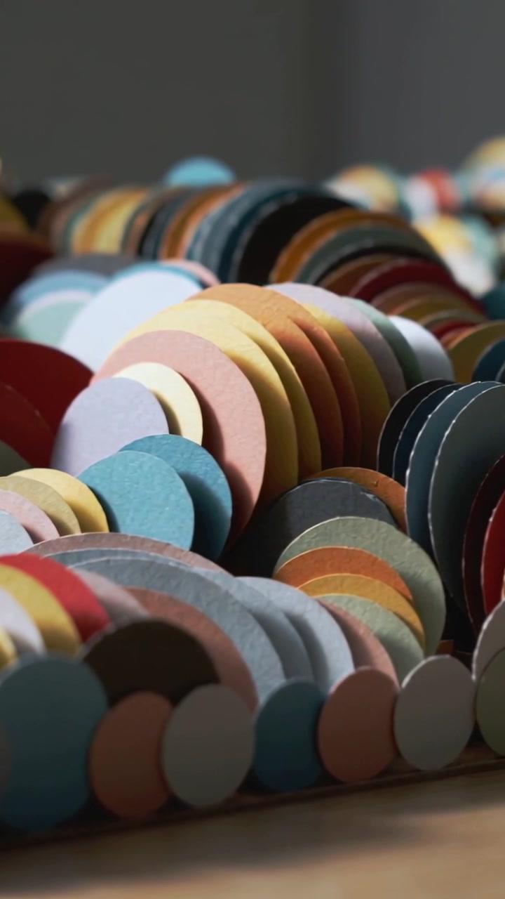 Vertical video: Panning camera revealing layered paper discs on wooden tabletop, highlighting color