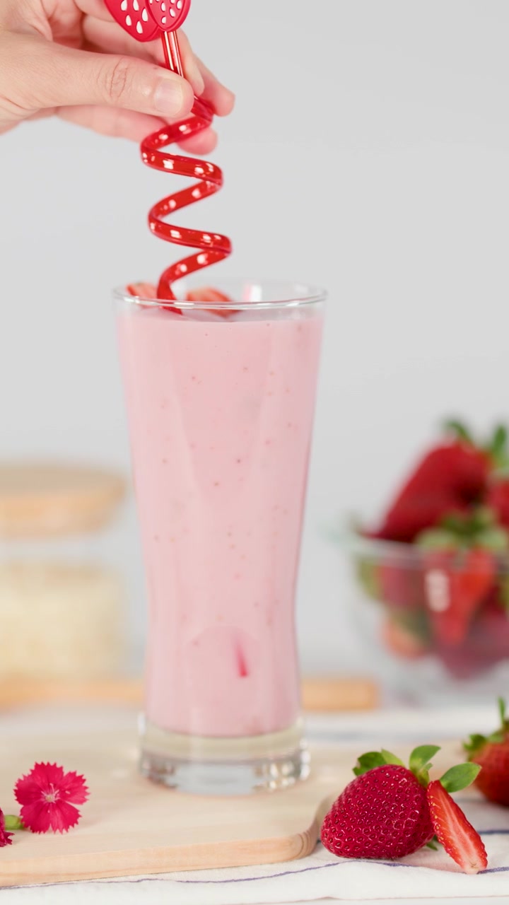 Una mano inserisce una cannuccia a spirale rossa in un cremoso milkshake rosa alla fragola, illuminazione brillante da studio, sfondo colorato.