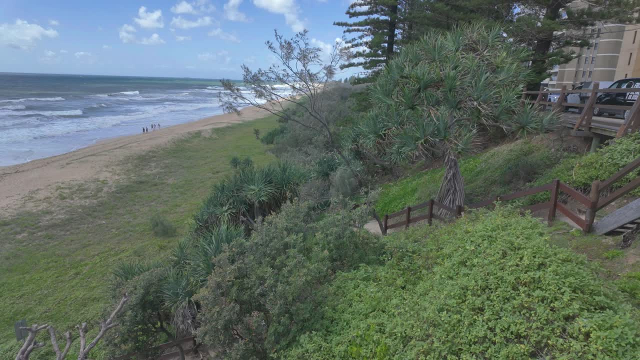 4K video of a beautiful sandy beach with people exercising, walking and green vegetation in the foreground