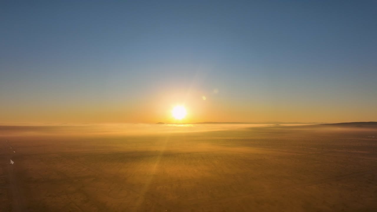 Sunrise over a serene landscape with light fog, warm golden tones bathing the scene, aerial