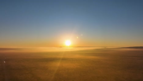 sunrise over a serene landscape with light fog, warm golden tones bathing the scene, aerial