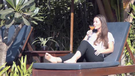 medium shot of a young lady relaxing on a sun lounger by the pool drinking a cocktail at a tropical hotel