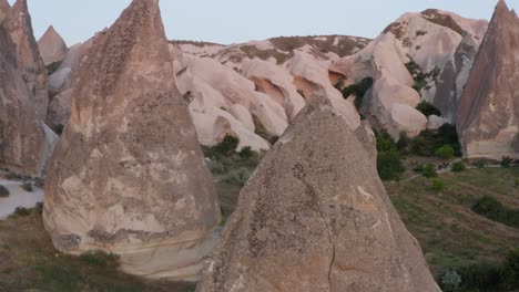 rotation around close-up of fairy chimney natural rock formation above grass fields to reveal landscape in cappadocia turkey