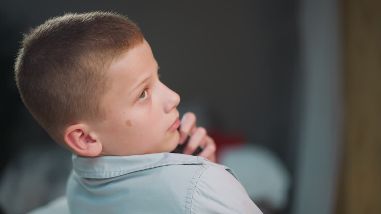 школьник звонит матери по телефону, поворачивая голову в сторону.