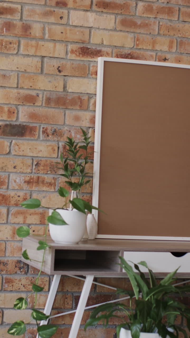 Vertical video of white frame and plants on desk with copy space against brick wall