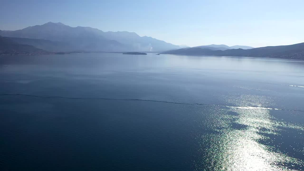 산이 있는 해안을 향해 만을 가로지르는 공중 영상과 깨끗한 물을 가로질러 항해하는 보트가 있습니다