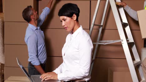 Warehouse-manager-working-on-laptop-with-staff-behind-her