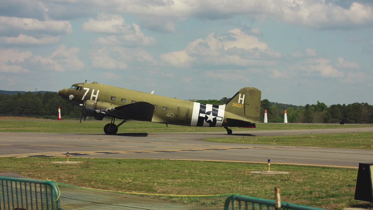 Eski bir C-47 askeri nakliye uçağı, bir havaalanı pisti üzerinde taksi yapıyor.
