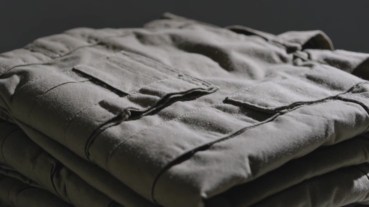 Showing folded khaki jacket with 2nd layer in studio, camera zooming, light raking, showing seams