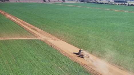 Vista-Aérea-De-Un-Tractor-Y-Una-Pequeña-Niveladora-Moviéndose-A-Lo-Largo-De-Un-Camino-De-Tierra-En-Una-Granja-De-Cultivos