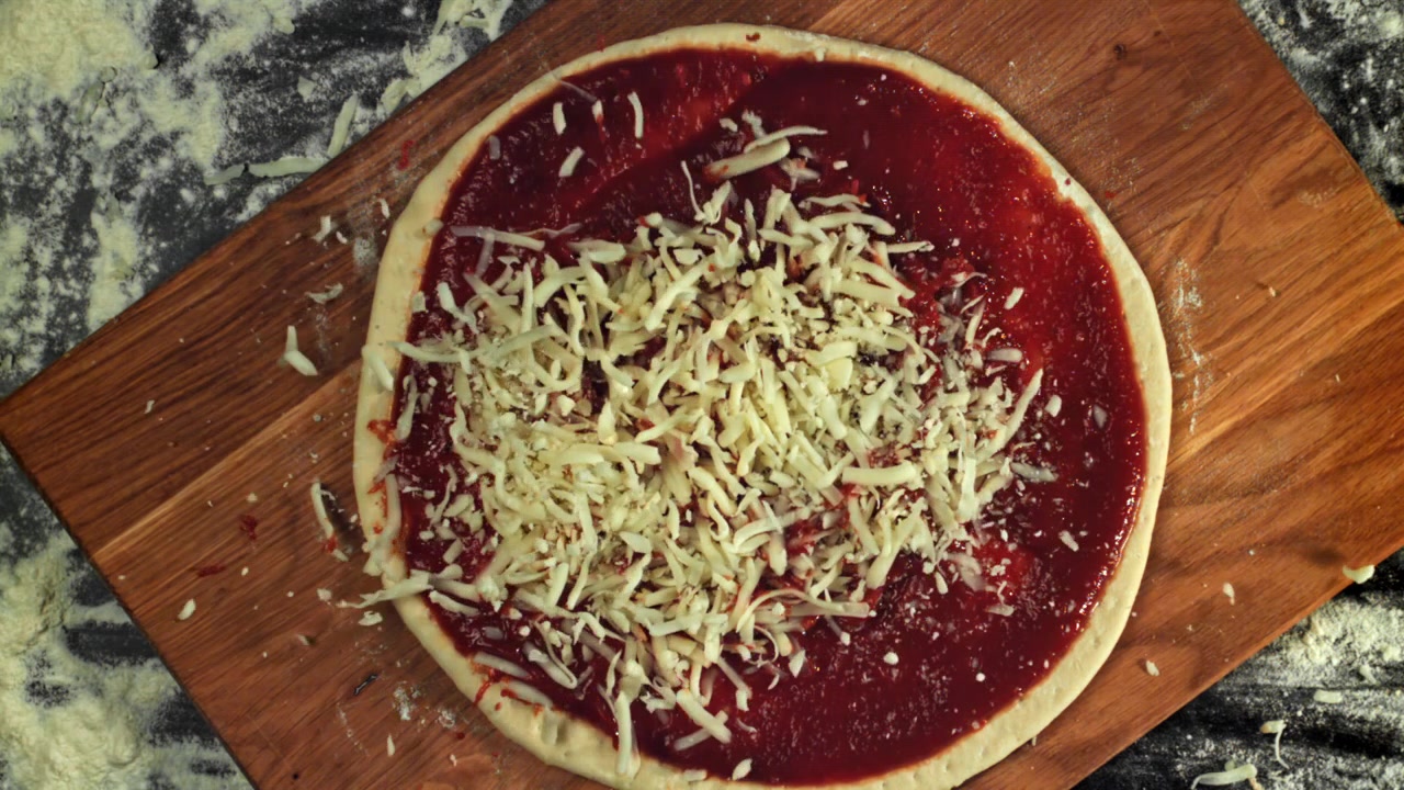 Mozzarella sfilacciata che cade su impasto per pizza con salsa di pomodoro