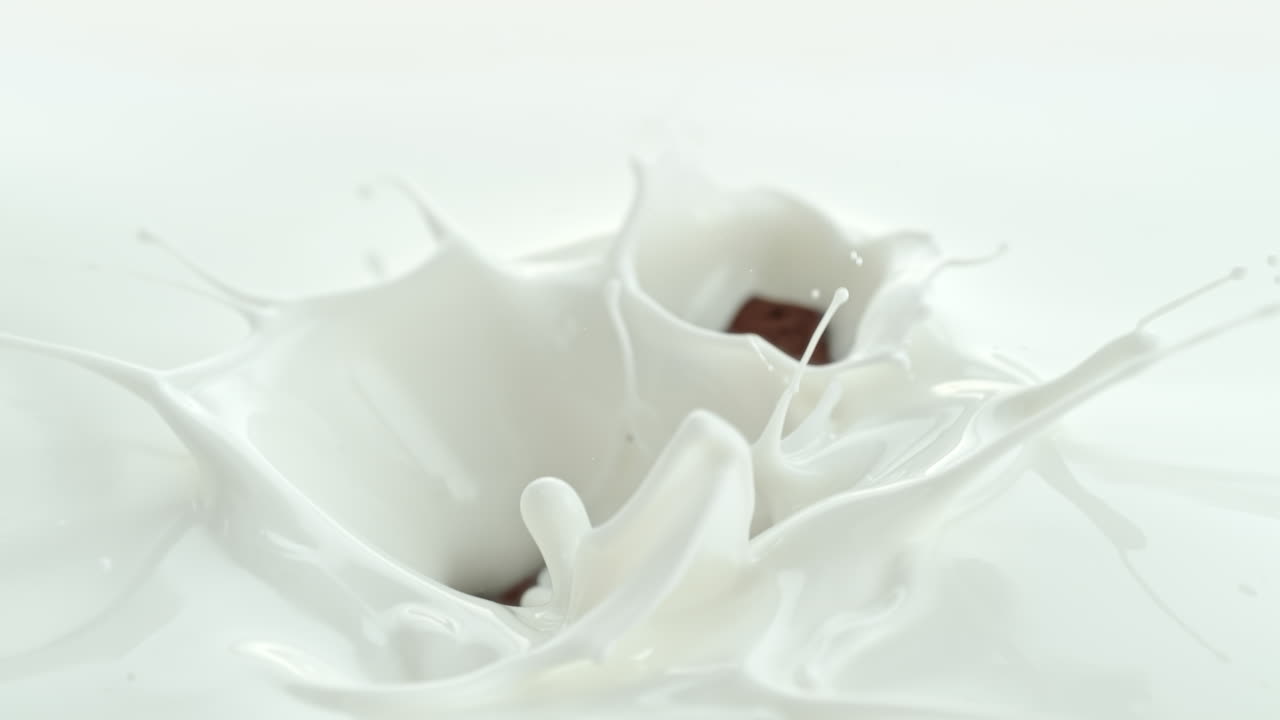 шоколадные кусочки падают в сливочное молоко, делая вихревые брызги в макро и замедленном движении