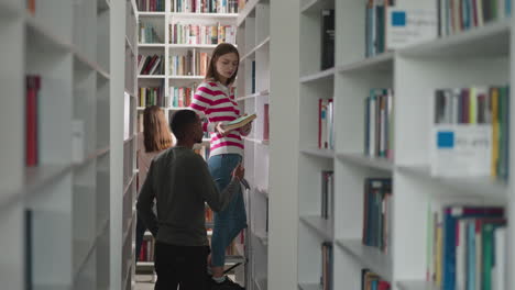 librarian gives book to man in public library. woman standing on step ladder helps male visitor to find literature in bookstore. university storage