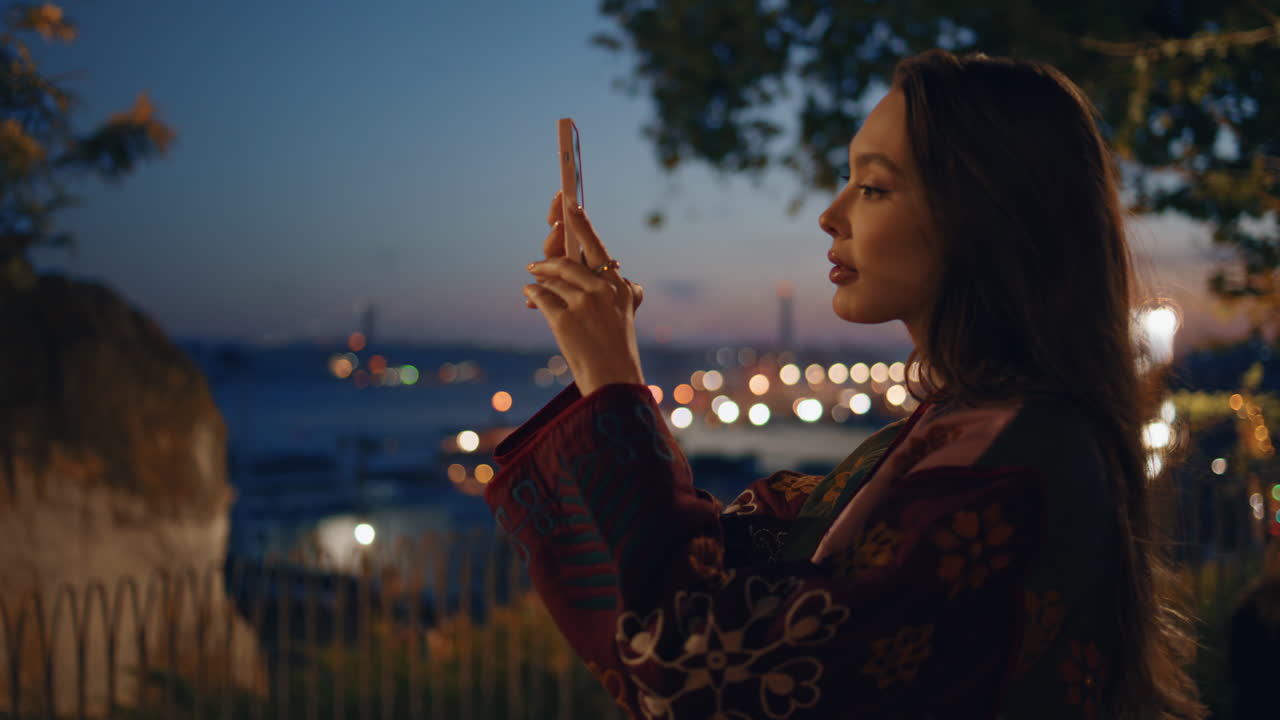 una mujer tomando una foto panorámica de la ciudad del crepúsculo desde la plataforma de observación del parque de cerca.