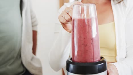 sección media de una pareja caucásica preparando batidos saludables en la cocina, cámara lenta
