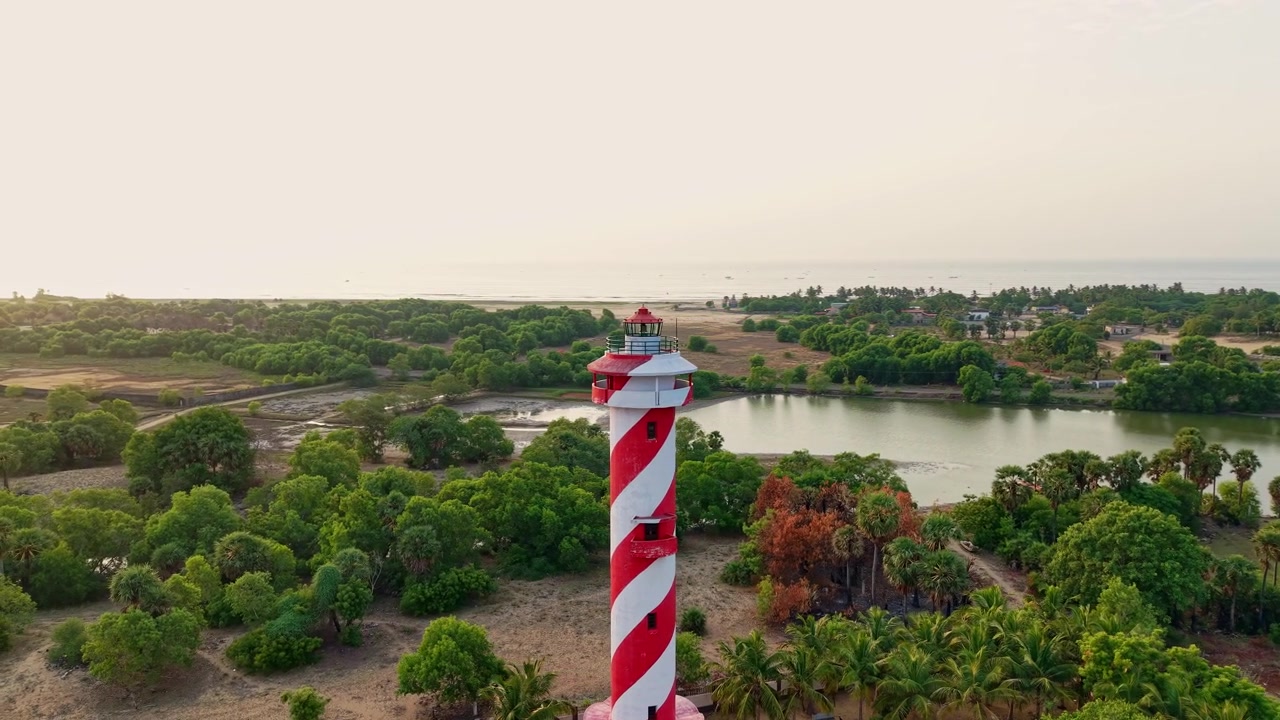 Vista aerea con drone di un faro a strisce che si affaccia sulle lagune interne vicino alla costa di Chennai con vegetazione lussureggiante e il Golfo del Bengala durante una serena alba