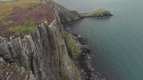 drone-shot-coast-cliff-landscape-in-beautiful-isle-of-skye-scotland,-green-grass-and-calm-sea