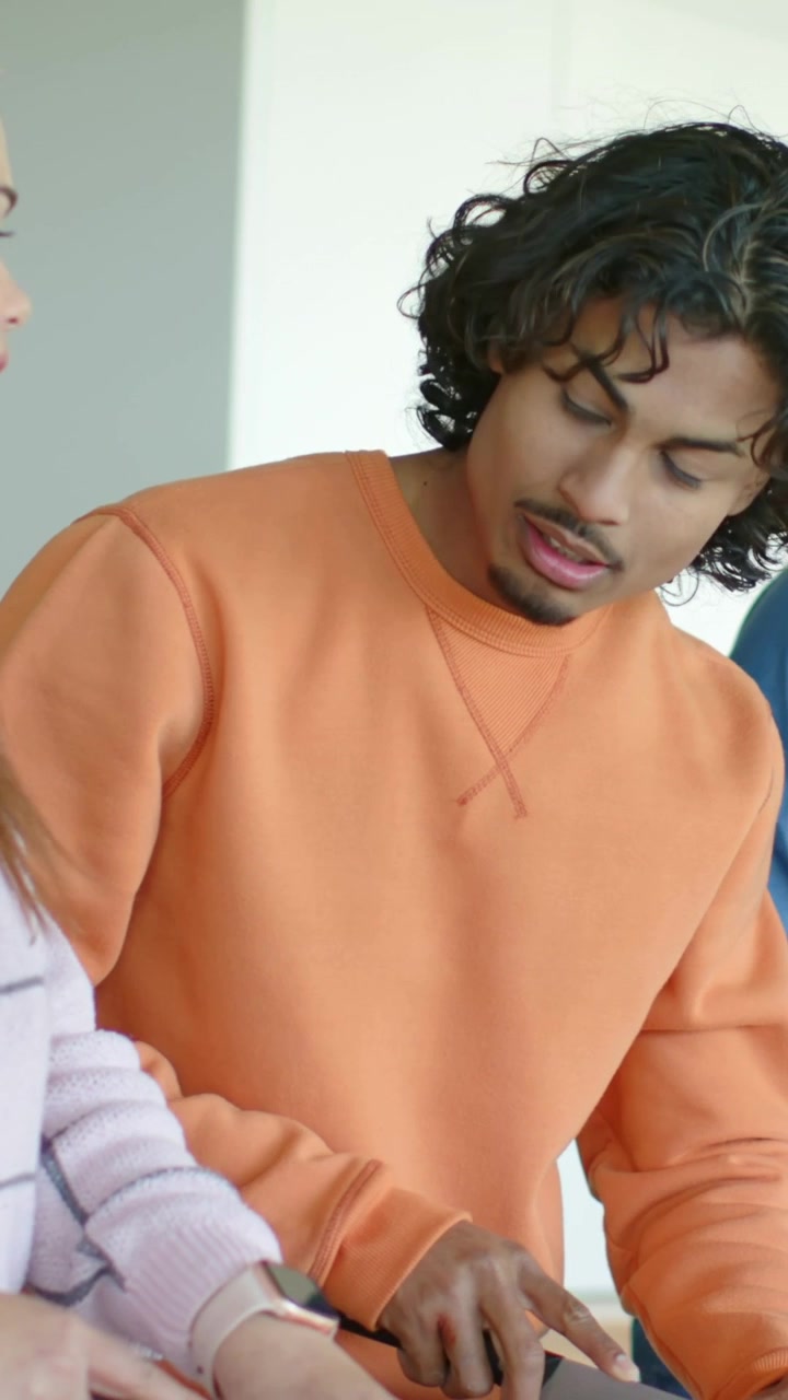 Vertical video: Starting meal, man in orange slicing tomato on board with chef knife, glancing