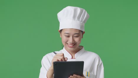close up de una mujer asiática cocinera tomando nota en una tableta mientras está de pie en el estudio de fondo de la pantalla verde