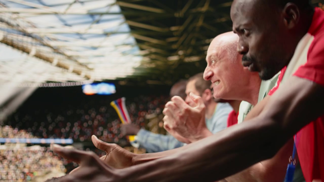 Tifosi di calcio della squadra rossa che reagiscono con gesti ansiosi sugli spalti dello stadio.