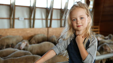 portrait of caucasian little girl in hat looking and smiling at camera in stable wih sheep flock