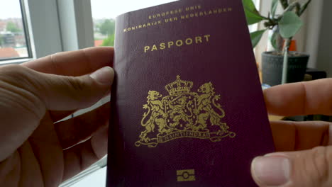 holding a dutch passport in two hands and rotating it.