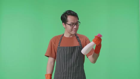 asian male housekeeper with an apron looking at spray in hand then showing thumbs up gesture to camera in the green screen studio