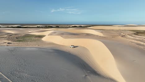 tracking drone shot of white suv with sand dunes in lencois maranhenses national park during the day in maranhao state, northeastern brazil