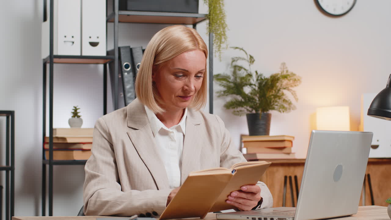 성숙한 사업가 여성이 흥미로운 책을 읽고 웃으며 문학을 즐기고 일 후 휴식을 취하고 있습니다.