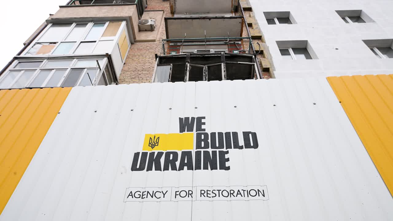 A metal fence reading "We Build Ukraine" by the State Agency for Reconstruction surrounds a building damaged by Russian missiles during the Ukraine-Russia war in Irpin, Ukraine.