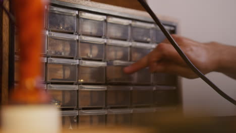 man takes metal rivet from small plastic drawer in workshop