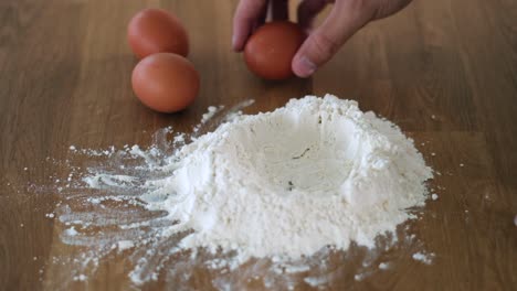 man cracking open an egg inside a mountain of flour