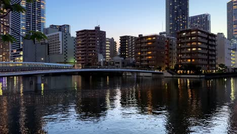 Cityscape-reflected-in-a-river-during-twilight-with-illuminated-buildings