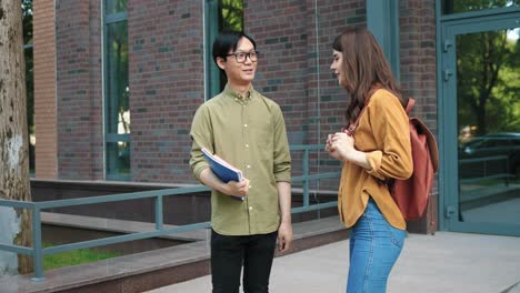 asian man talking with his caucasian female classmate in the street near the college