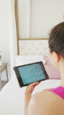 vertical video of asian woman using tablet with smart home panel in bedroom, in slow motion