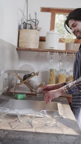 vertical video of biracial man washing dishes in kitchen, slow motion