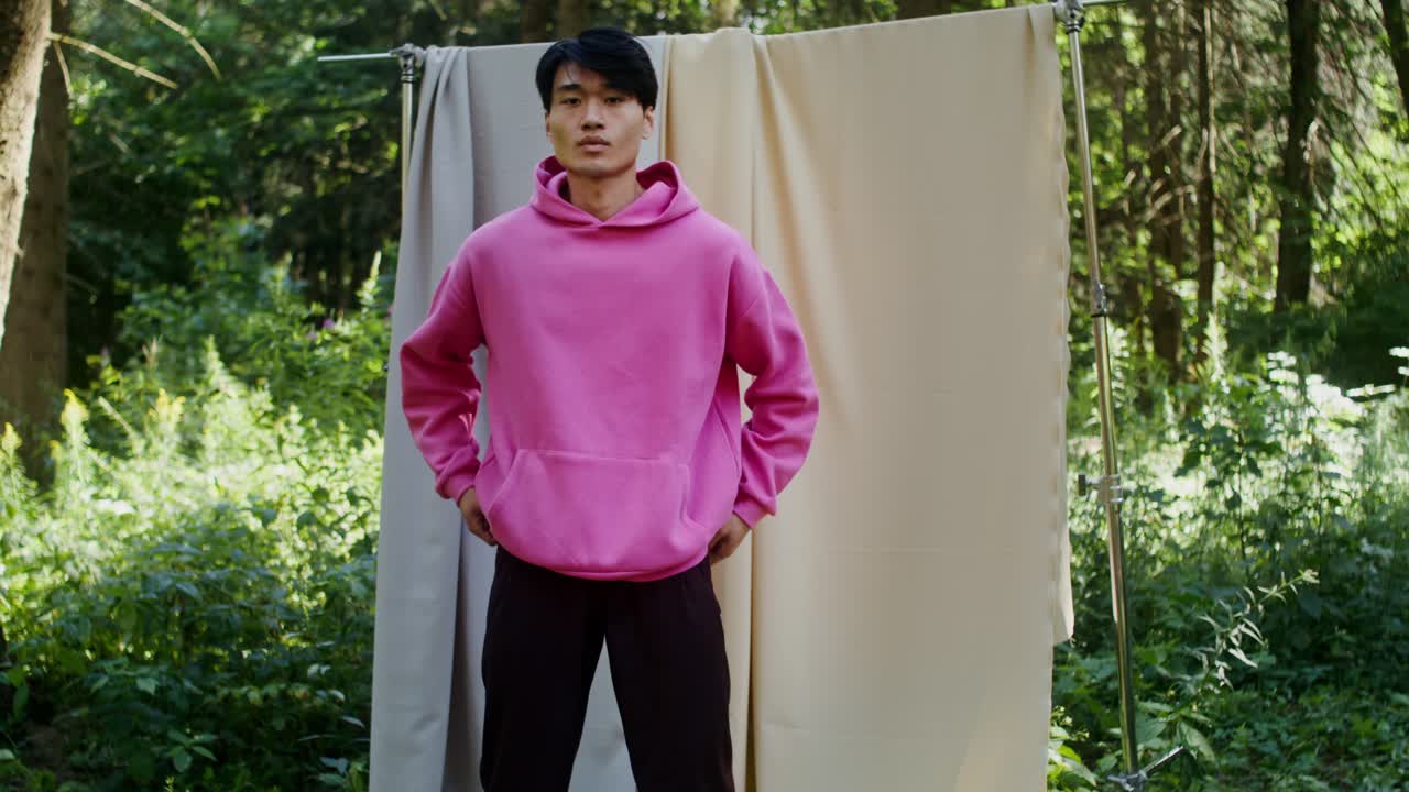 Man in pink hoodie posing in a forest