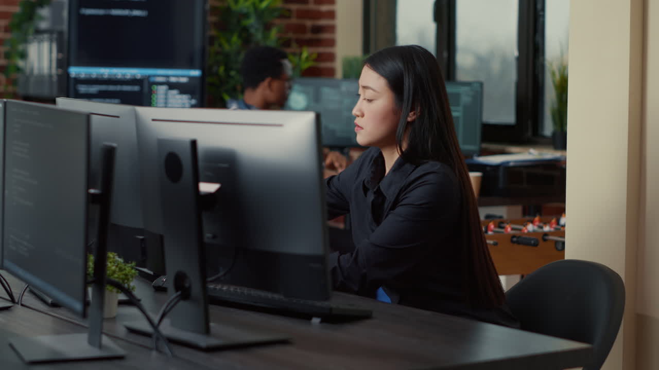 Asiatischer Softwareentwickler kommt an den Schreibtisch, setzt sich und hält einen Laptop mit Programmieroberfläche