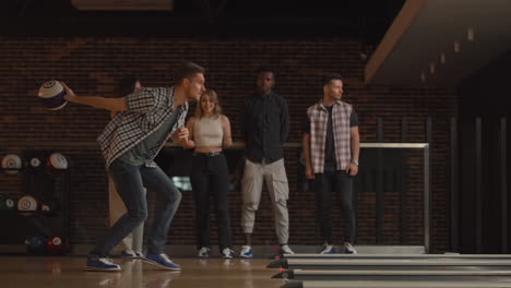 a young man makes the final throw with a bowling ball and wins the game with the support and joy of his friends of different nationalities. rejoice and celebrate the victory