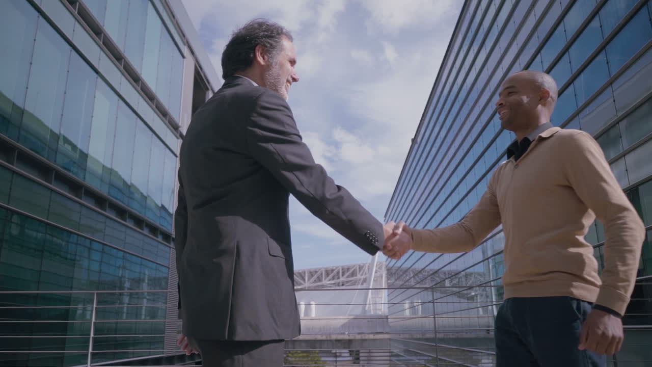 Manager sorridenti che si stringono la mano durante un incontro vicino all'edificio per uffici