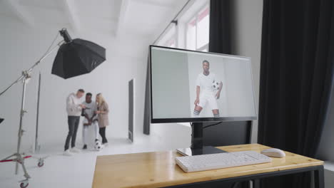 monitor con una portada publicitaria de la imagen en el fondo un fotógrafo un jugador de fútbol un modelo y un director miran fotos de una sesión de fotos para la portada en una cámara