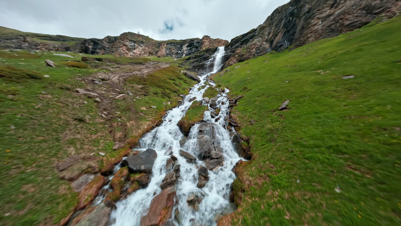 cascada de montaña en cascada a través de colinas verdes exuberantes bajo un cielo nublado cerca de cervinia