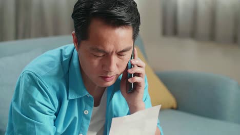 close up of asian man with a laptop answering the call and having headache while looking at the bill in hand