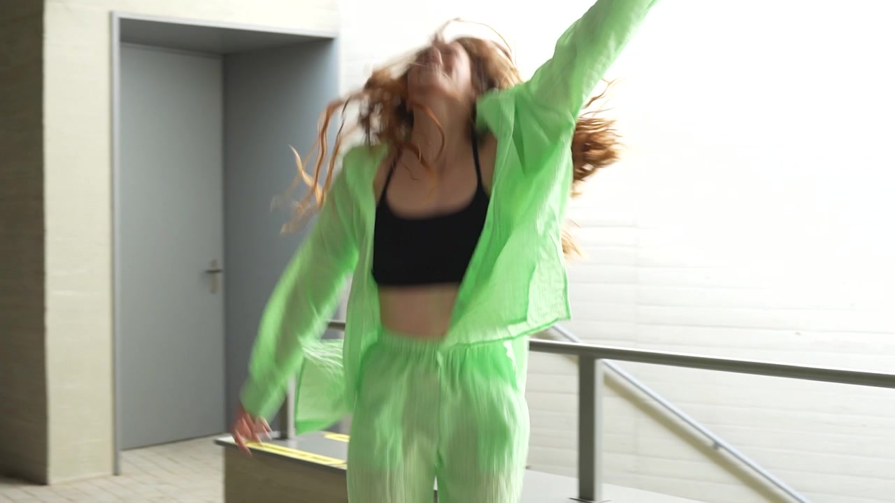A joyous redhead dances energetically in a vibrant green tracksuit in a modern urban environment