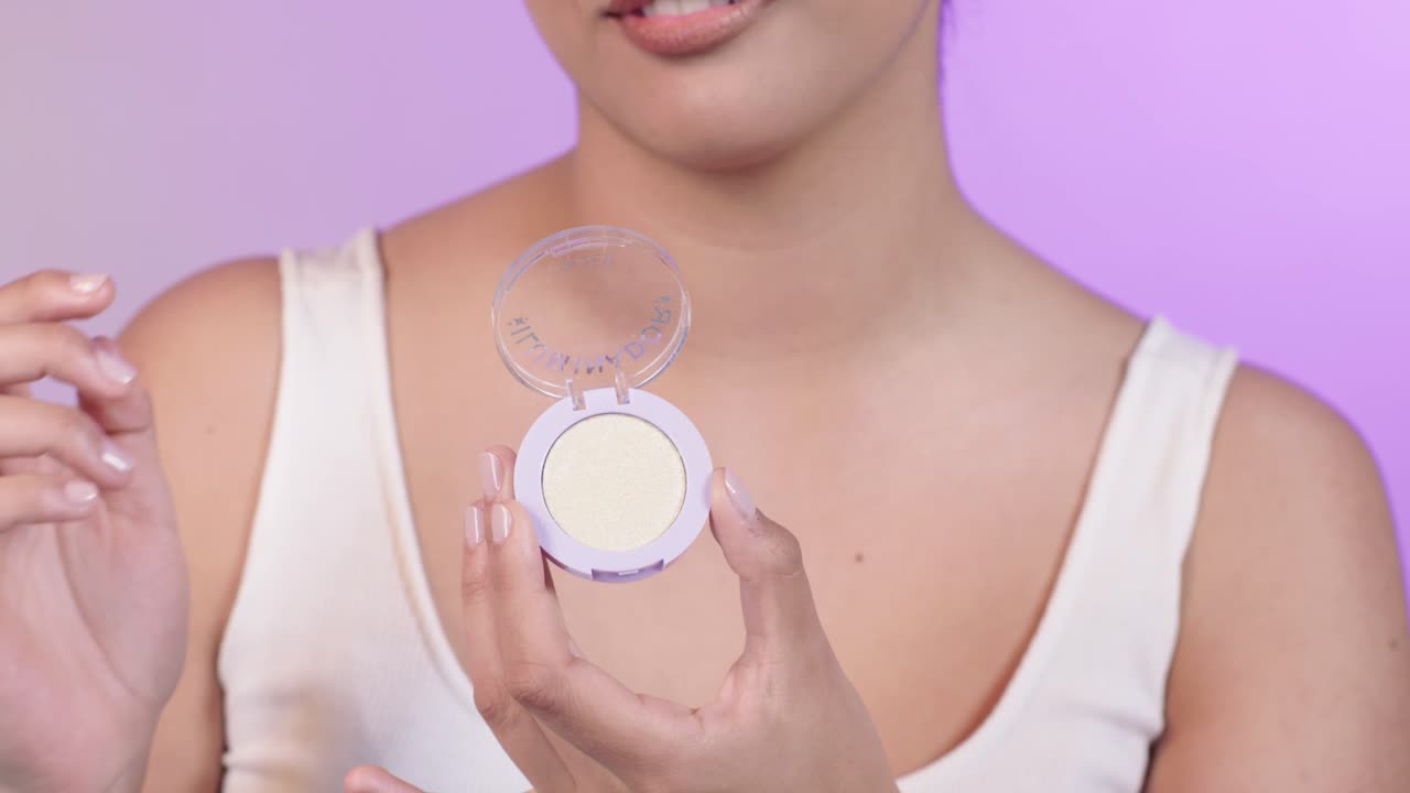 Close up of a beautiful young woman picking up highligher with her fingers and smiling, make up, cosmetics, on a pink background