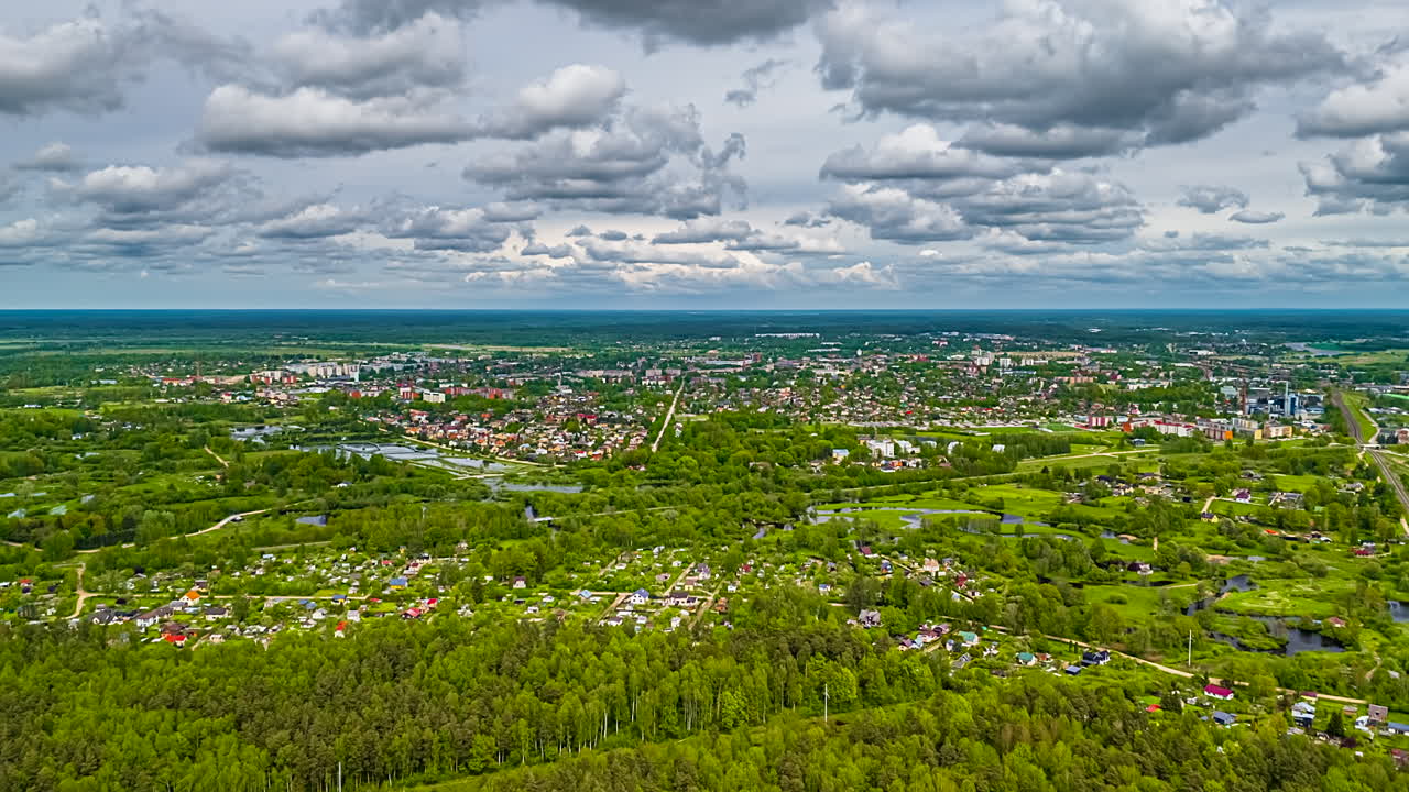 Aerial hyperlapse over forest and village with train tracks and flowing clouds.
